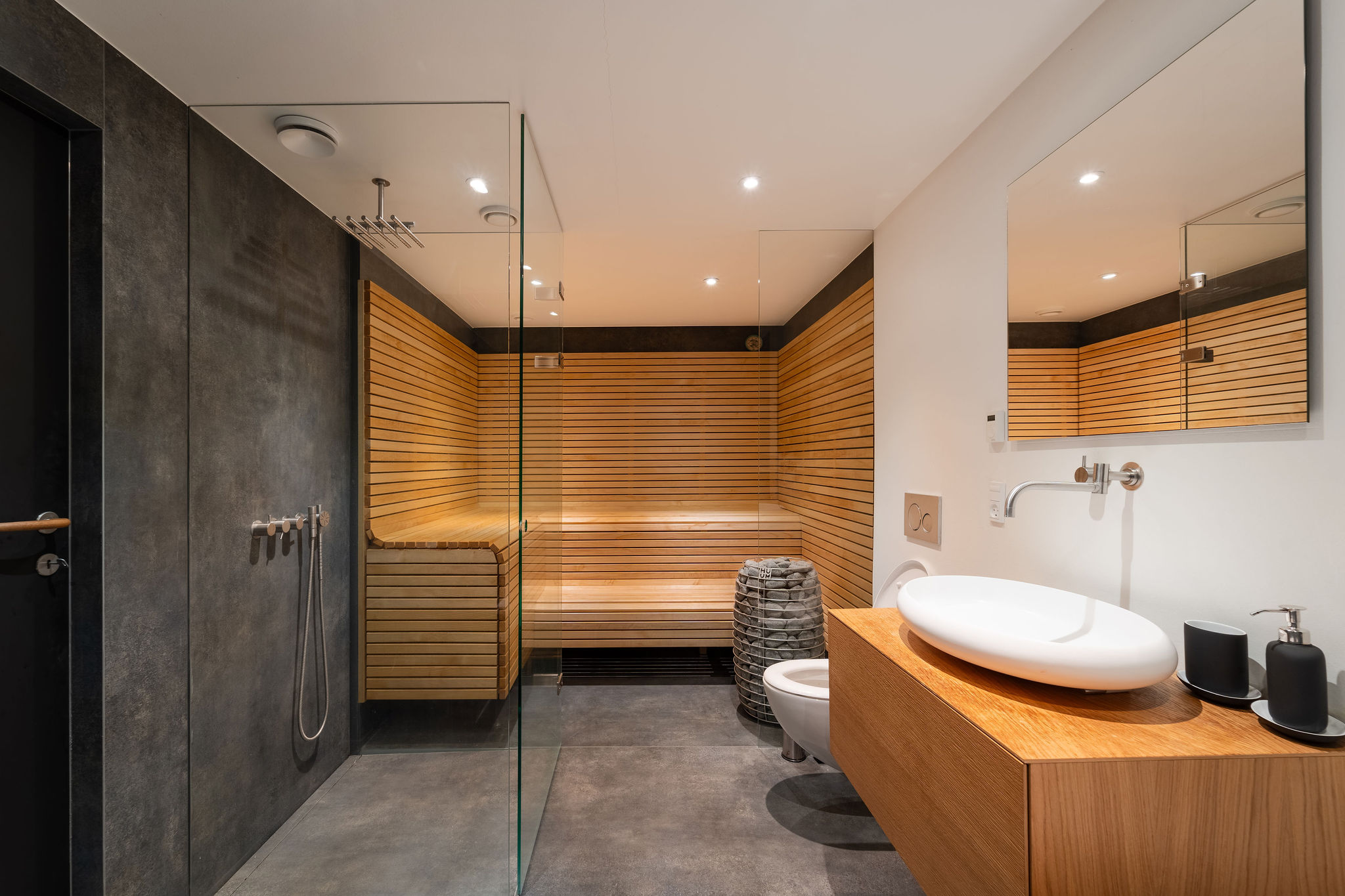 Wellness-rum med stort sauna i lyst trælatte, glasbruser med rainshower og egetræsbordplade med oval vask