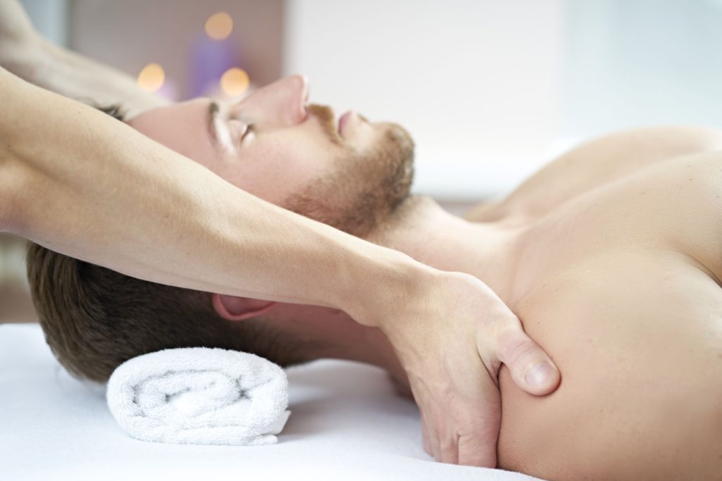 Mand modtager skulder- og armmassage på behandlingsbrik, øjne lukkede, stearinlys i baggrunden
