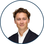 Rundt beskåret profilfoto af ung mand med mørkt krøllet hår i marineblå blazer og hvid skjorte, smiler mod kameraet